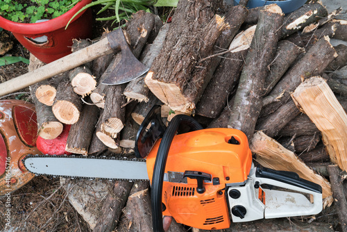 Professional gasoline powered chainsaw on piles of cut wood.