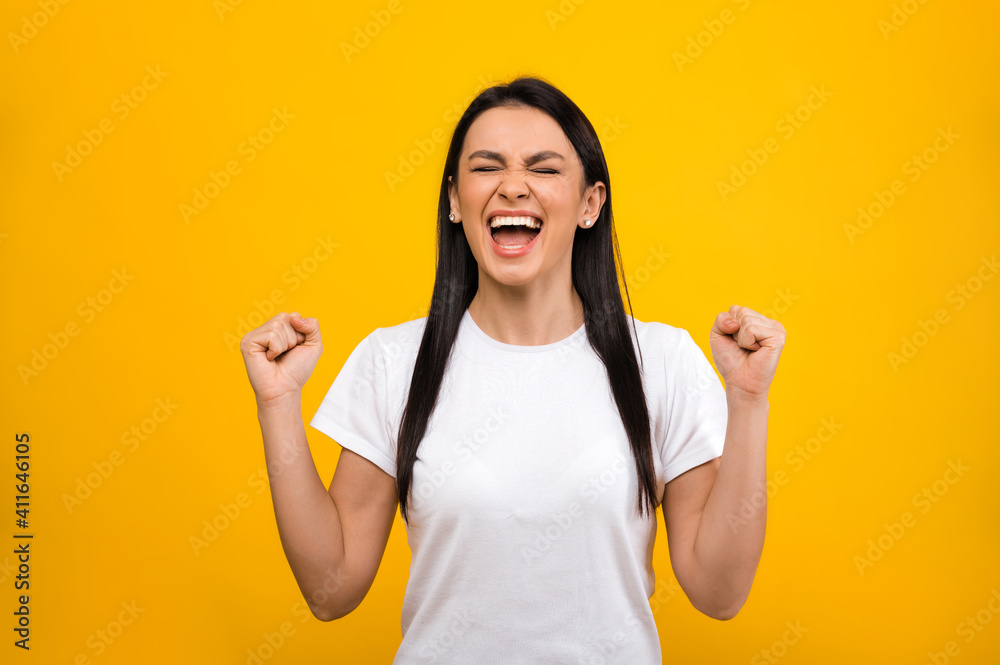 Happy joyful caucasian girl wearing basic white t-shirt, rejoicing in success or winning, standing on blue isolated background
