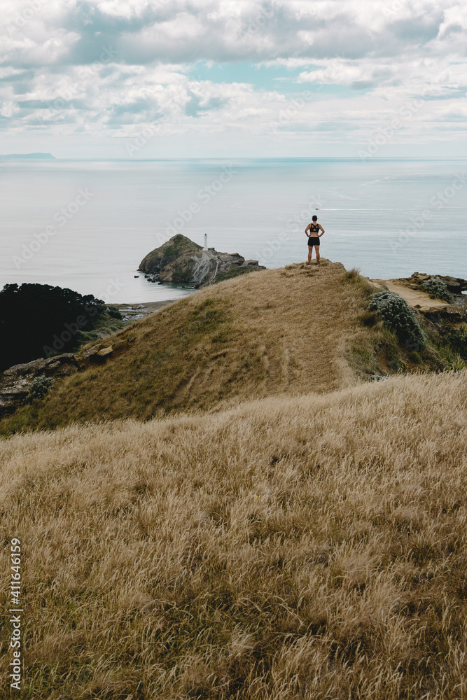 Woman conquering the top of Castle Rock mountain and looking at Castle Point lighthouse. New Zealand