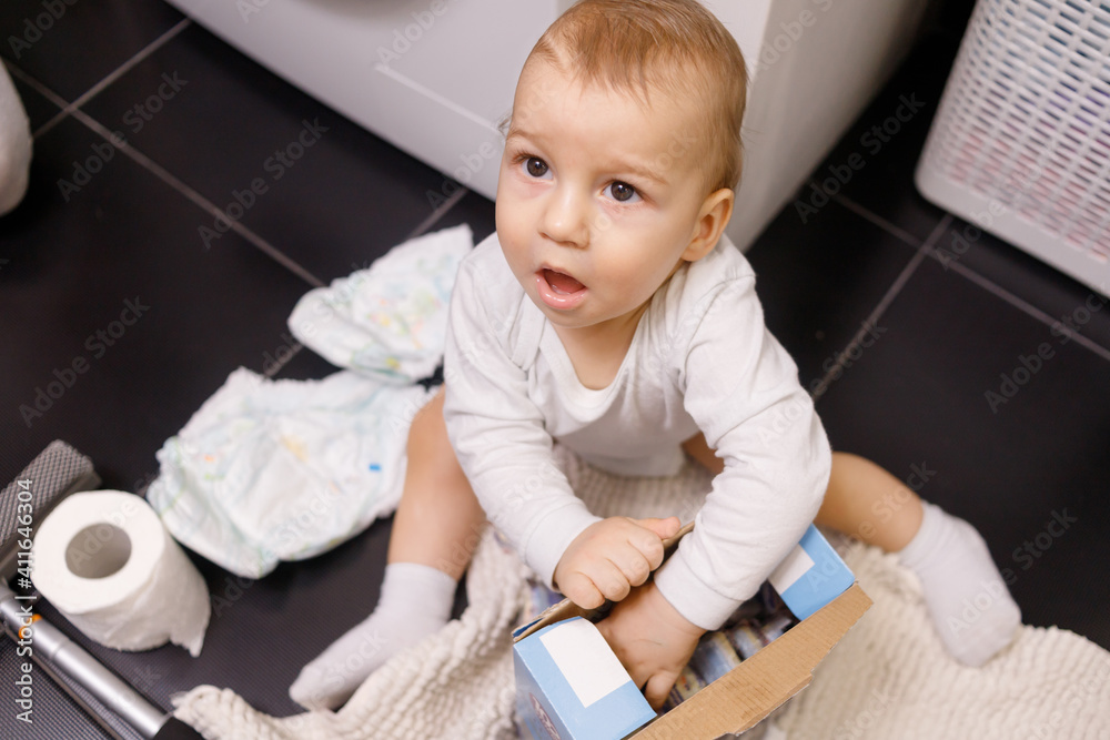 Infant boy open box with tablet for dishwasher or detergent in bathroom alone Infant boy open box with tablet for dishwasher or detergent in bathroom alone