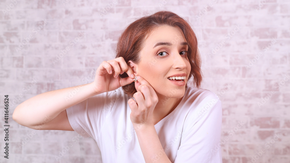 a beautiful smiling woman adjusts her earring in front of the mirror a beautiful smiling woman adjusts her earring in front of the mirror
