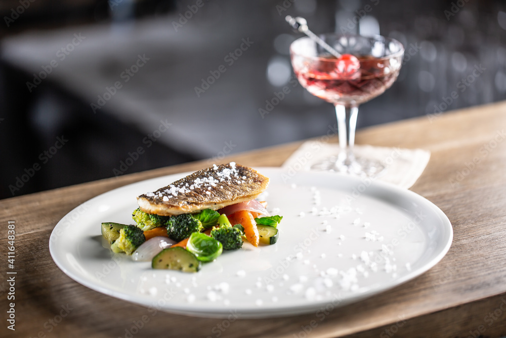 Healthy fish cooked with steamed vegetables served on a plate next to a negroni cocktail Healthy fish cooked with steamed vegetables served on a plate next to a negroni cocktail
