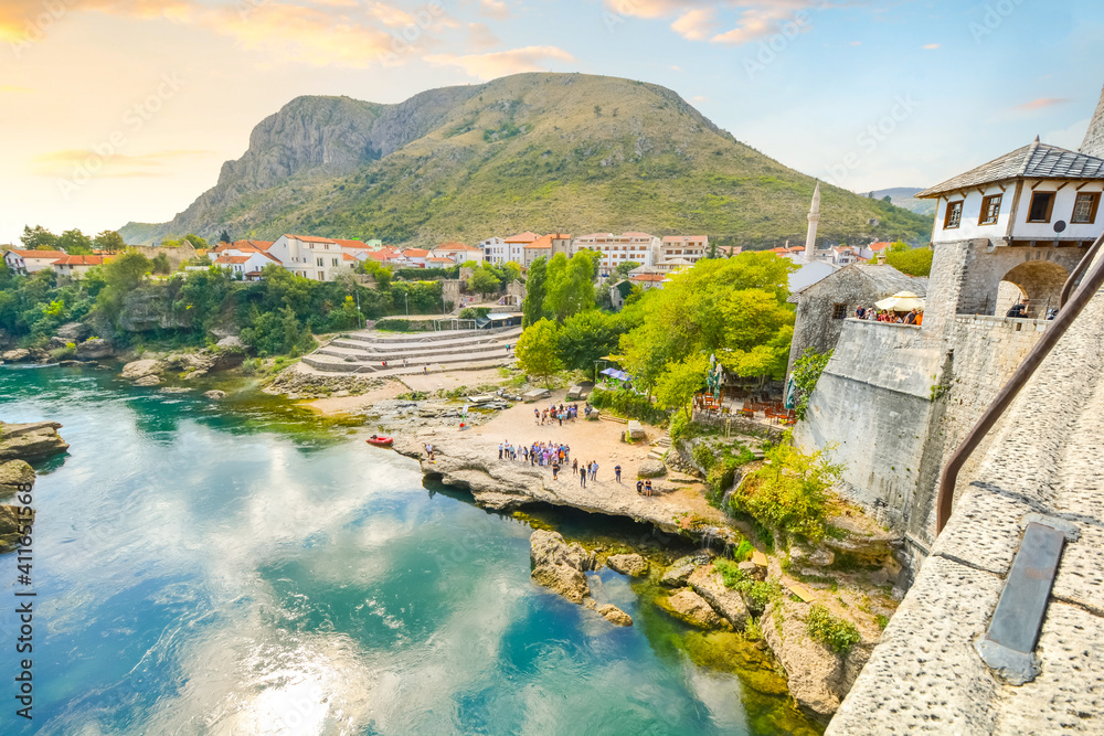 View of the Neretva River and tourists on the shore from atop the old Mostar Bridge in Mostar Bosnia and Herzegovina at sunset.