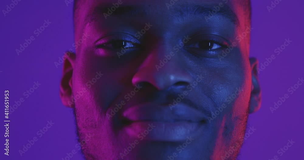 Close up portrait of african american man looking at camera in neon light and smiling