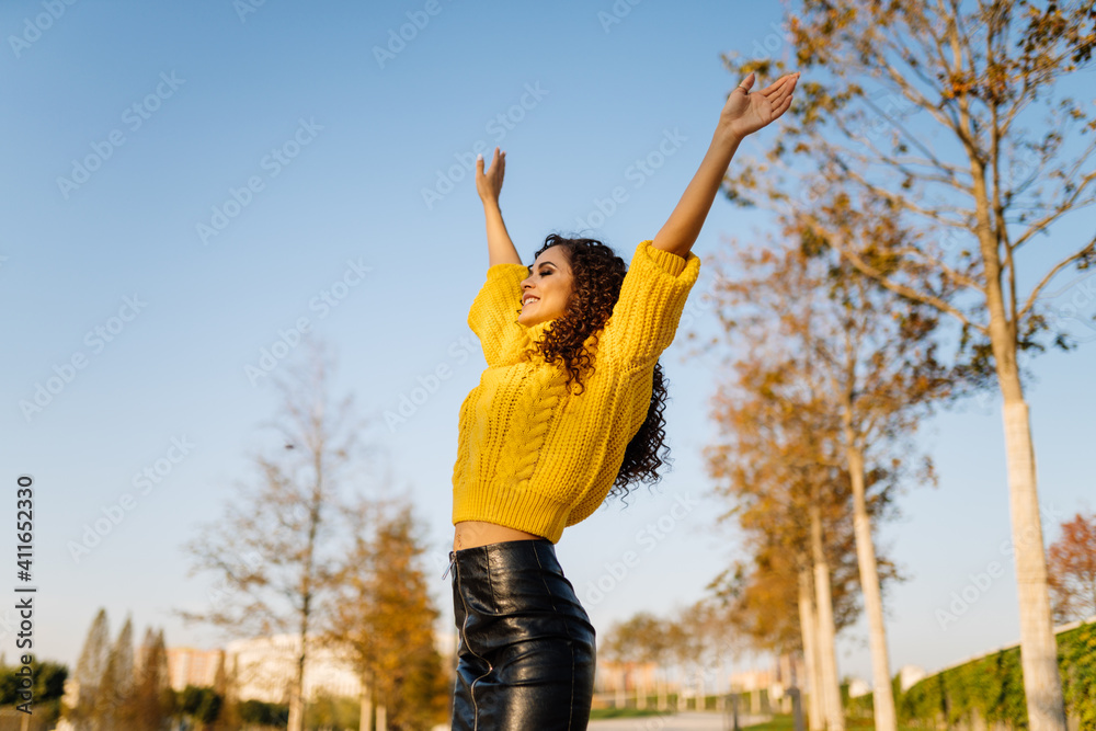 In the autumn park, the model dressed in a bright yellow sweater and black leather skirt with an expression of bliss on her face lifted up her arms and stretched her bare stomach. High quality photo
