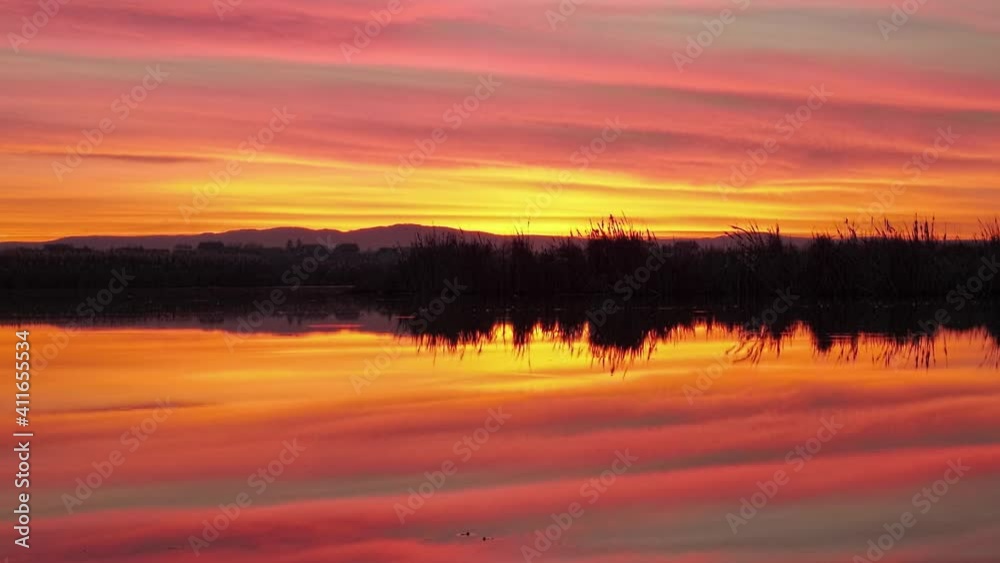 Beautiful orange sky reflected in water. Gold sunset over the lake background. Ripple waves on water surface.