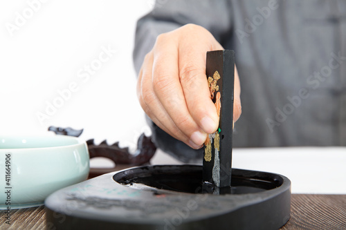 The calligrapher is studying ink on the inkstone with ink sticks in hand