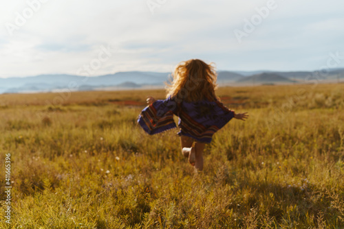 A red-haired girl runs at sunset in a field against the backdrop of the mountains. Unrecognizable silhouette. High quality photo