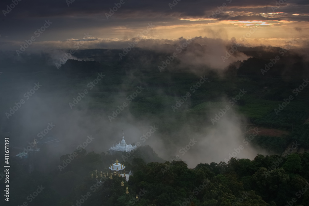 White Buddhist pagoda complex on a hill top in a green forest at sunrise time