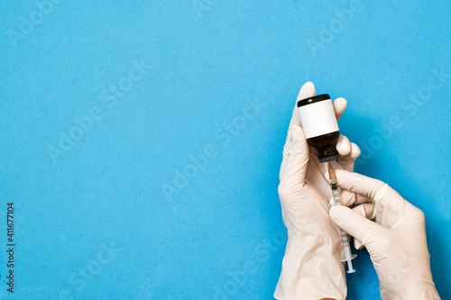 Hands in a white gloves withdrawing liquid with syringe from the Coronavirus Vaccine vial on blue background. Space for text. Suspended Covid-19 vaccine test.  Flat lay