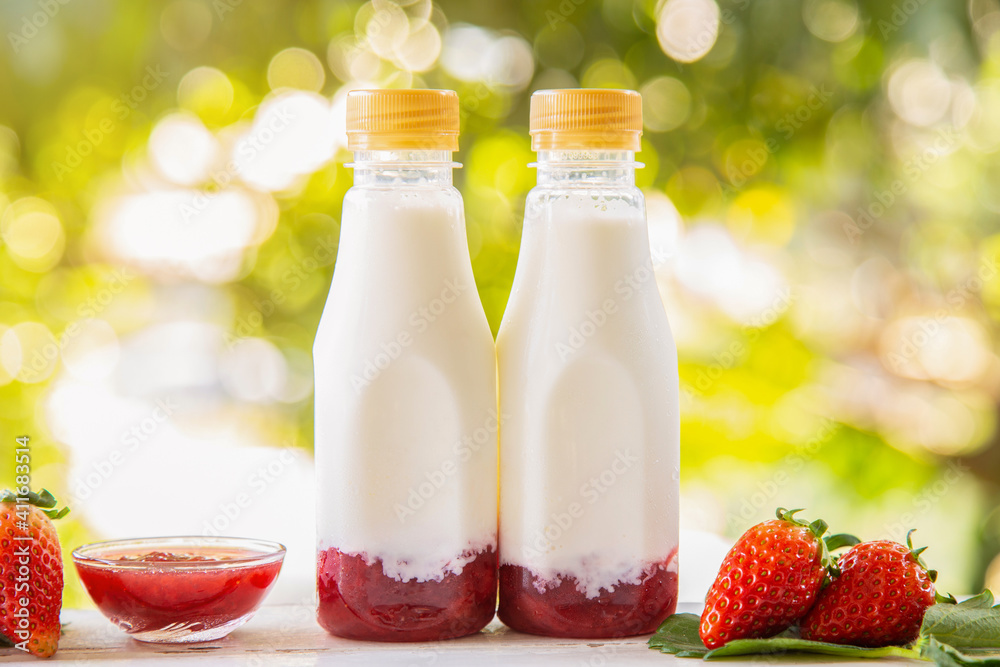 Homemade strawberry milk in a bottle on white wooden table with strawberry fruits with nature background Homemade strawberry milk in a bottle on white wooden table with strawberry fruits with nature background