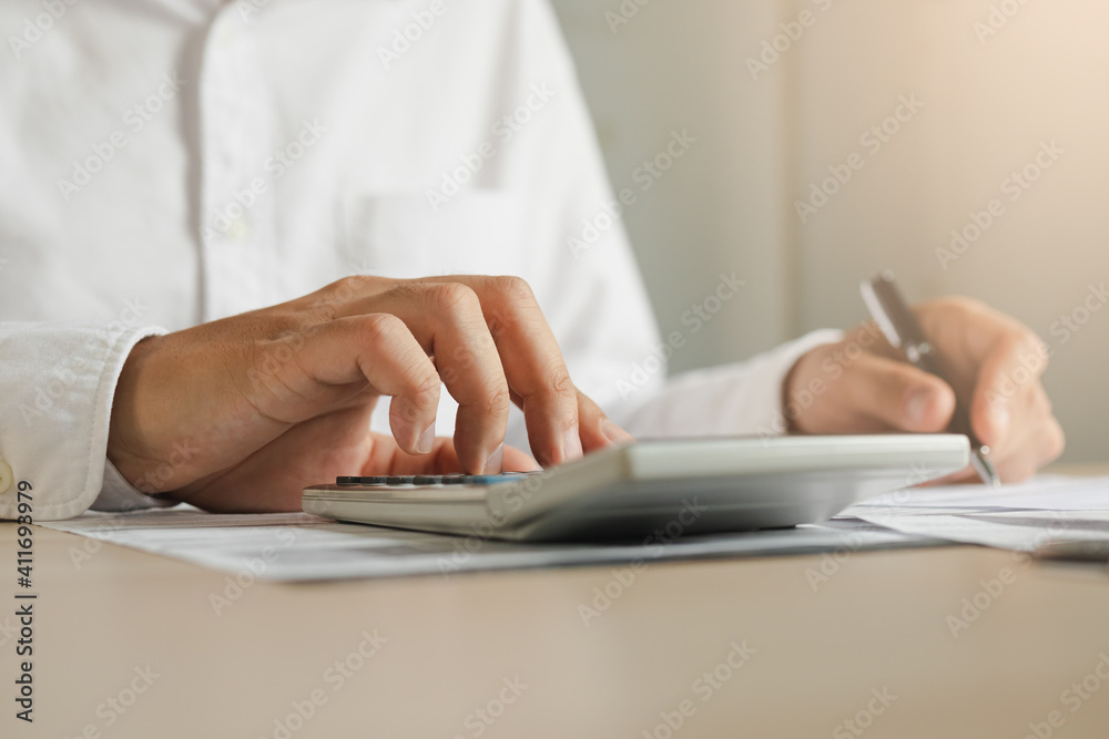 Close up hand of young asian businessman, male is pressing a calculator to calculate cost from invoice, bills or statement to plan his spending for payment, payday at home. Finance people concept. Close up hand of young asian businessman, male is pressing a calculator to calculate cost from invoice, bills or statement to plan his spending for payment, payday at home. Finance people concept.