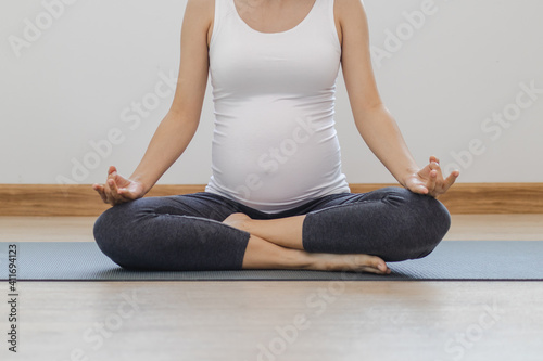 Pregnancy, Maternal young pregnant woman practice yoga in the lotus position, clam pose for pregnant to meditation, exercise on mat for wellbeing while rest at home. Healthy care for mother concept.