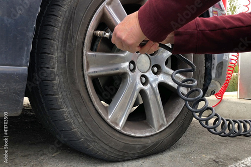 Close up of an older woman, female hands using automated air pump to inflate car tire with low pressure.