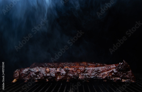 Smoke rolls off barbecue ribs slow cooking on a grill photo