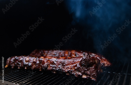 Babyback pork ribs smothered in sticky barbecue sauce slow cooking on a pellet grill smoker for a summer picnic