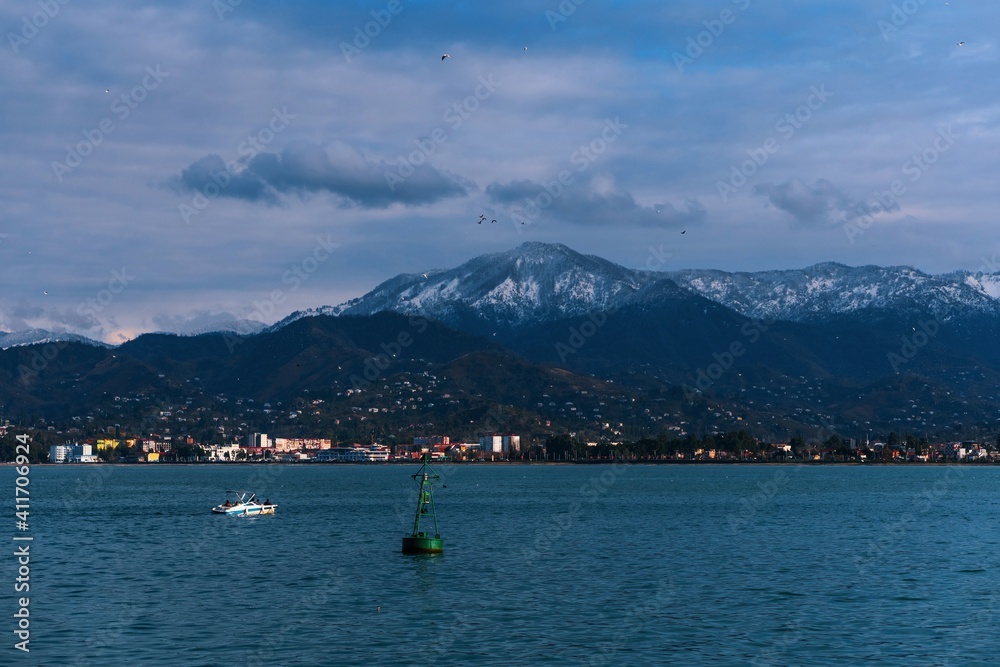 Beautiful landscape on the blue sea, mountains and clouds. A float sways on the waves at the port in Batumi, Georgia.
