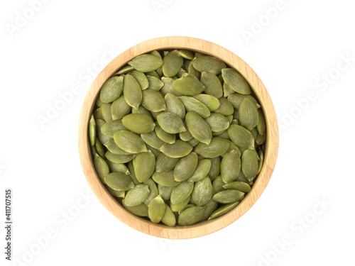 Organic pumpkin seeds in circle shaped wooden bowl top view isolated on white background. Organic pumpkin seeds healthy ingredients food concept.