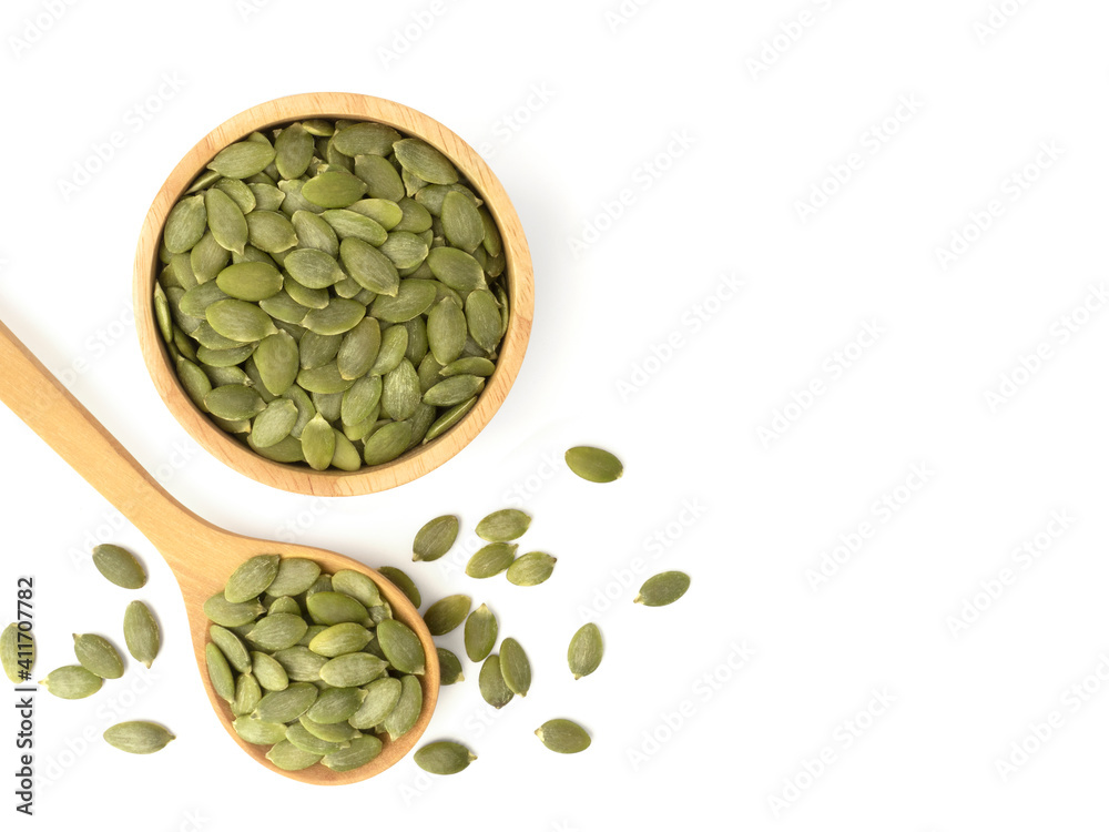 Fototapeta premium Organic pumpkin seeds in circle shaped wooden bowl with wooden spoon top view isolated on white background. Organic pumpkin seeds healthy ingredients food concept.