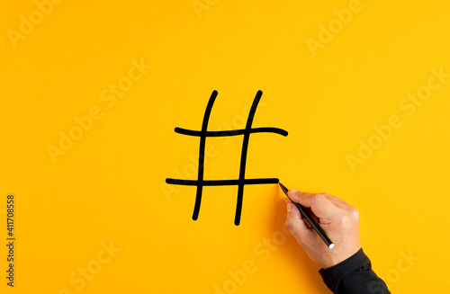 Male hand drawing a hashtag symbol on yellow background.