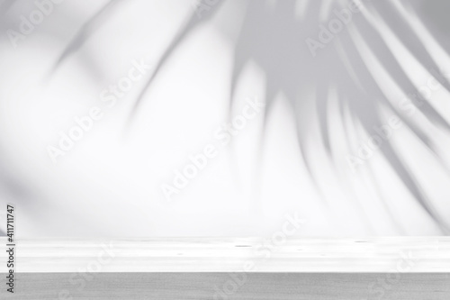 Empty wooden table with shadow of tropical leaves on background with copy space