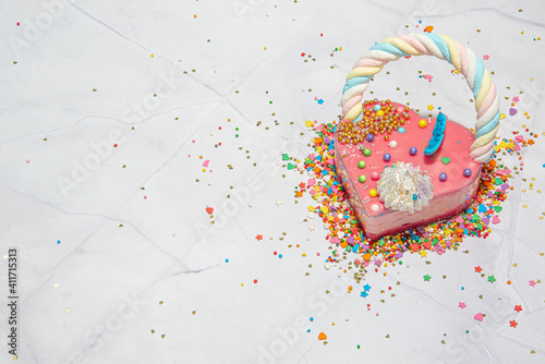 Pink heart shape cake on a white marble background with a lot of small colorful candies. Valentine day. About love. copy space. High quality photo