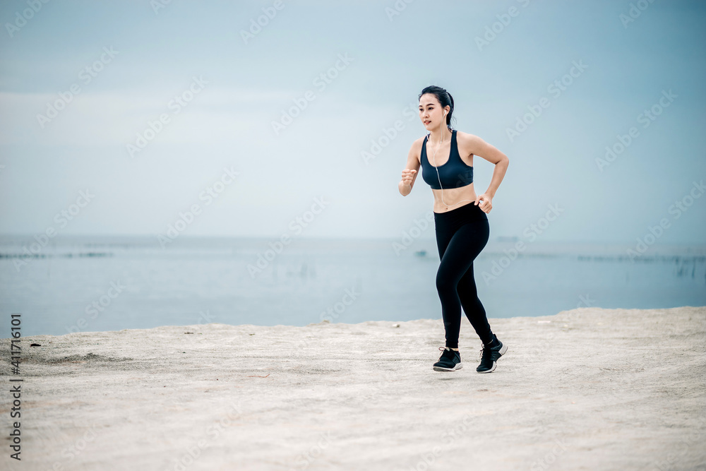 Asian fitness runner body closeup doing warm-up routine on beach before running, stretching leg muscles with standing single knee to chest stretch. Female athlete preparing legs for cardio workout.