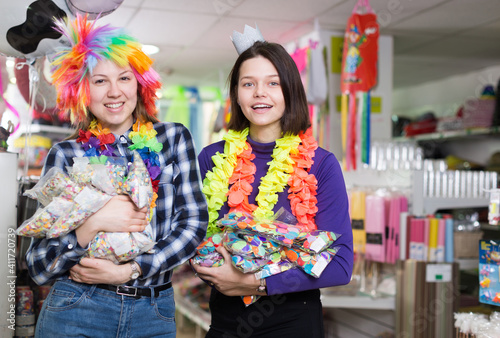 Cheerful young female friends with plastic bags of confetti having fun in festive things store