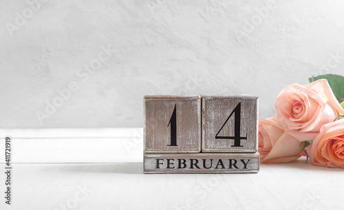 Wooden perpetual calendar on date February 14, bouquet of roses on a light background. Concept Valentine's Day. Copy space.