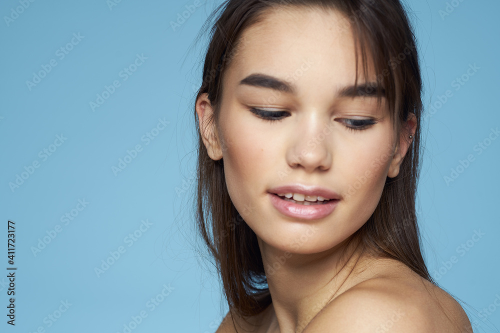 Obraz premium brunette with bare shoulders cosmetics close-up skin care blue background