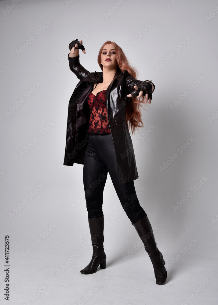 full length portrait of girl with long red hair wearing dark leather coat,  corset and boots.