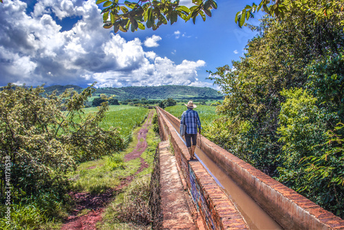 Campesino caminando sobre acueducto caña de azucar paisaje mexicano nubes cielo azul latinoamérica mexicano anciano viejo naturaleza verde campo de caña cultivo