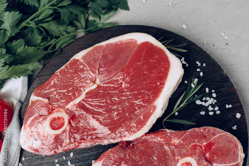 Raw rib-eye beef steak on wooden cutting board on gray background