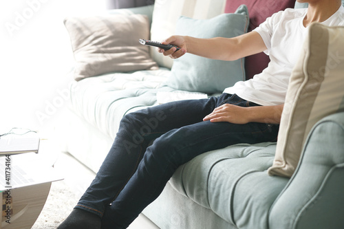 asian young man pressing TV remote button on sofa at home