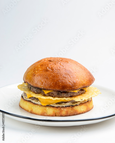 Giant perfect burger with ham and cheese served on a clear white plate over plain white background.
