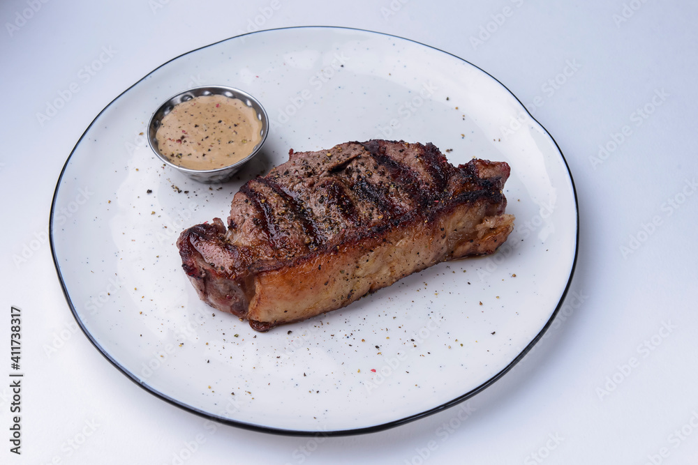 Delicious beef steak with sauce served on a white plate over white background. BBQ meat, barbecue concept.