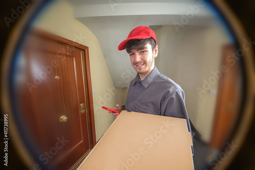 Delivery man delivering food order, pizza in cardboard box, seen through the peephole photo