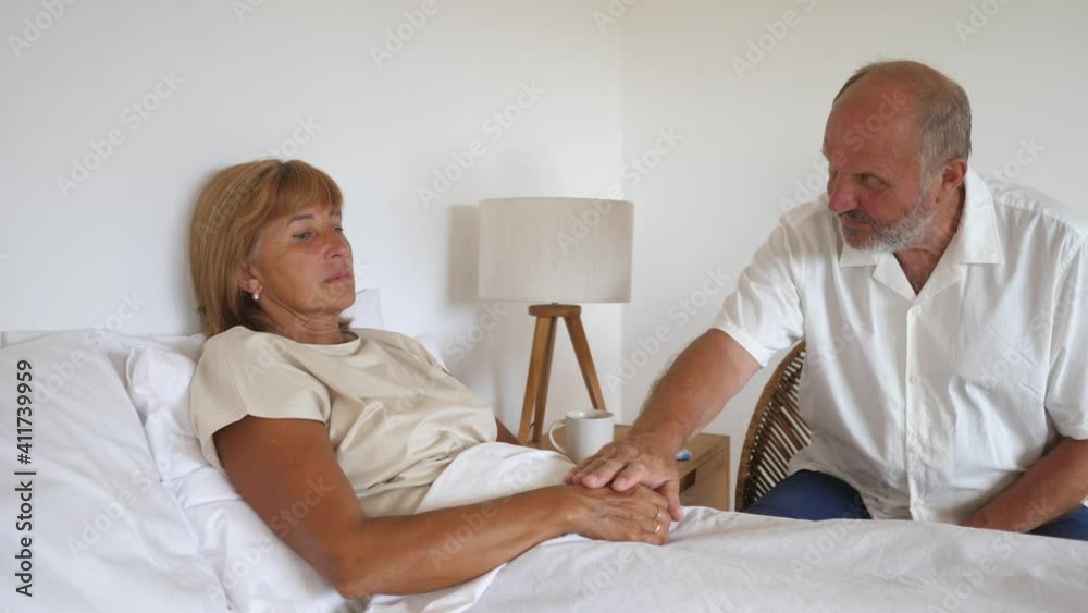 Emotional Support in middle aged couple. Husband holds hand of his sick wife lying down Emotional Support in middle aged couple. Husband holds hand of his sick wife lying down