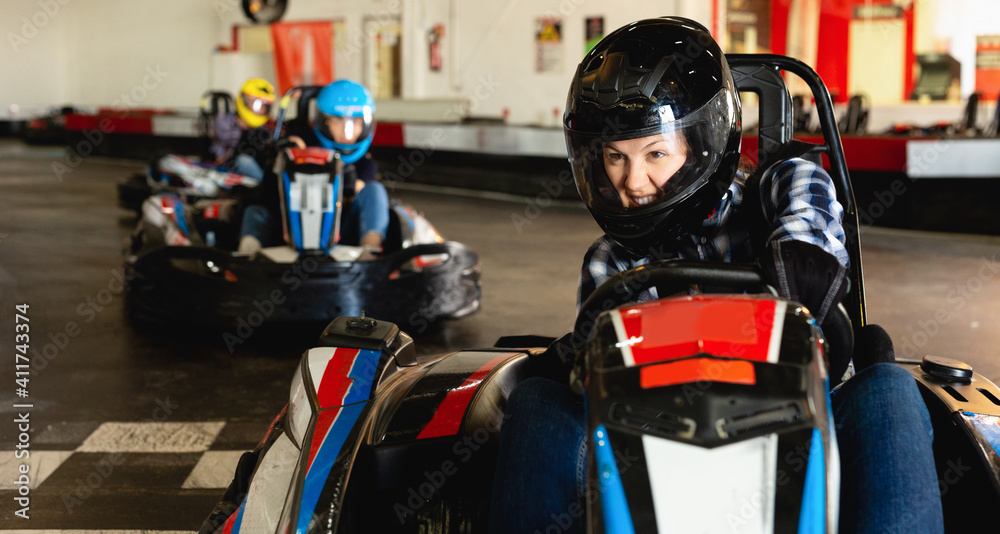 Glad positive girl and her friends competing on racing cars at kart circuit
