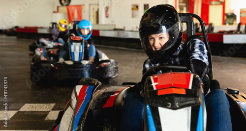 Glad positive girl and her friends competing on racing cars at kart circuit