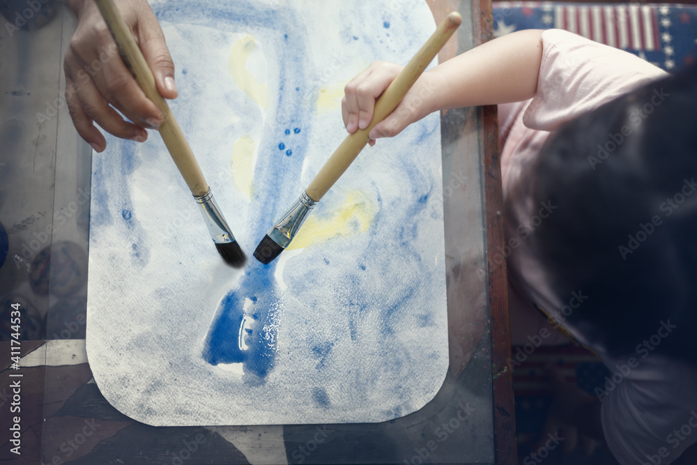 Top view of little girl and mother painting water colors together at home,selective focus.Background for art education and learn through play activity for kid development. Top view of little girl and mother painting water colors together at home,selective focus.Background for art education and learn through play activity for kid development.