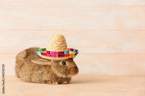 Cute fluffy rabbit with sombrero hat on light wooden background