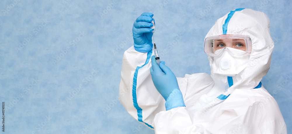 Medical worker in a white protective suit on a blue background. Wear a respirator and gloves. Prepares a syringe for a vaccine set. Place for an inscription. Panorama.
Medical worker in a white protective suit on a blue background. Wear a respirator and gloves. Prepares a syringe for a vaccine set. Place for an inscription. Panorama.