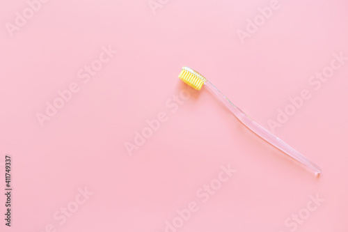 Toothbrush with yellow bristles on a pink background. Oral hygiene, dentistry, teeth cleaning concept. Minimalism, top view, copy space. © Ольга Холявина