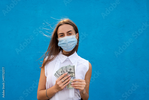 business young woman wear espiratory mask holding dollar bills isolated blue background photo