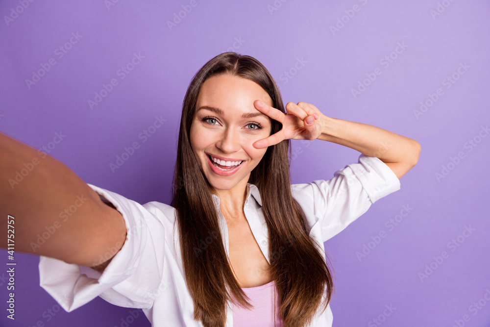Photo of funny girl raise hand show v-sing near eye take selfie wear white shirt isolated purple color background