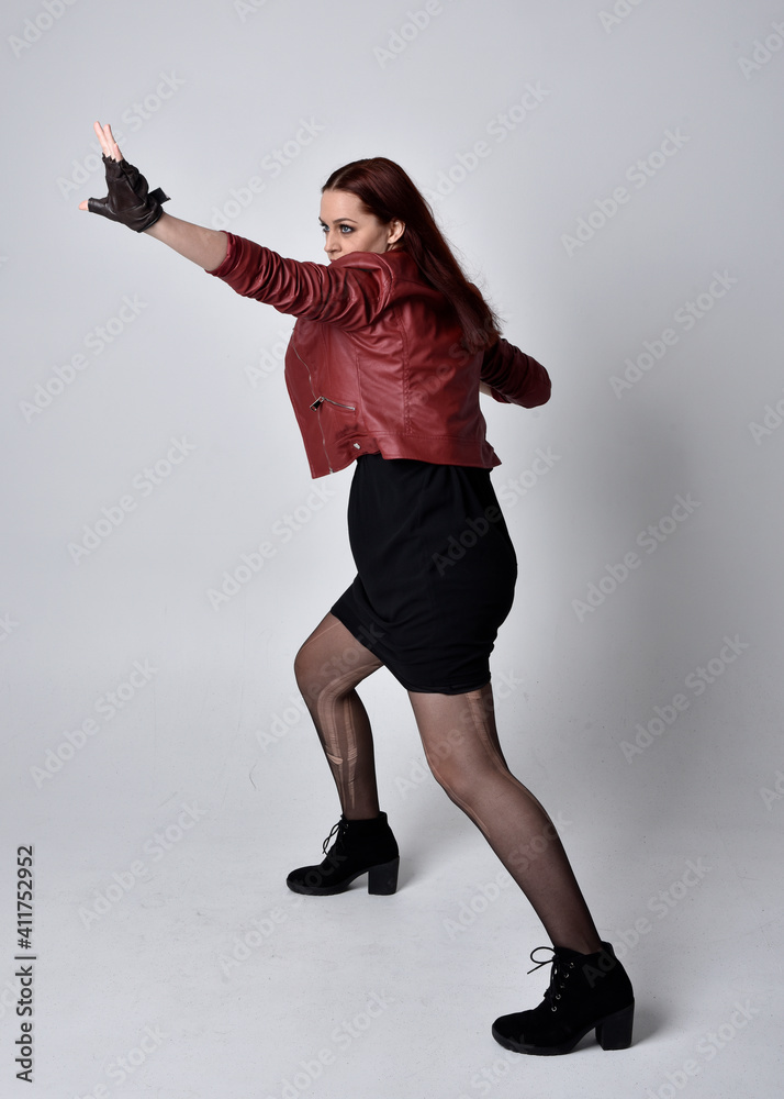 Full length portrait of girl wearing red leather jacket, tights with boots and gloves. Posing with gestural hand movements as if casting spell against a studio background. Full length portrait of girl wearing red leather jacket, tights with boots and gloves. Posing with gestural hand movements as if casting spell against a studio background.
