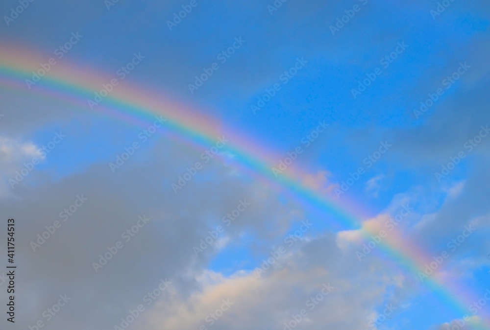Beautiful rainbow on the background of a blue sky with clouds.