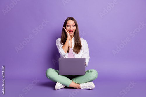 Photo portrait full body view of woman with laptop sitting in lotus pose isolated on vivid purple colored background