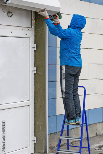 A man repairs the visor over the entrance to the store on a winter day
